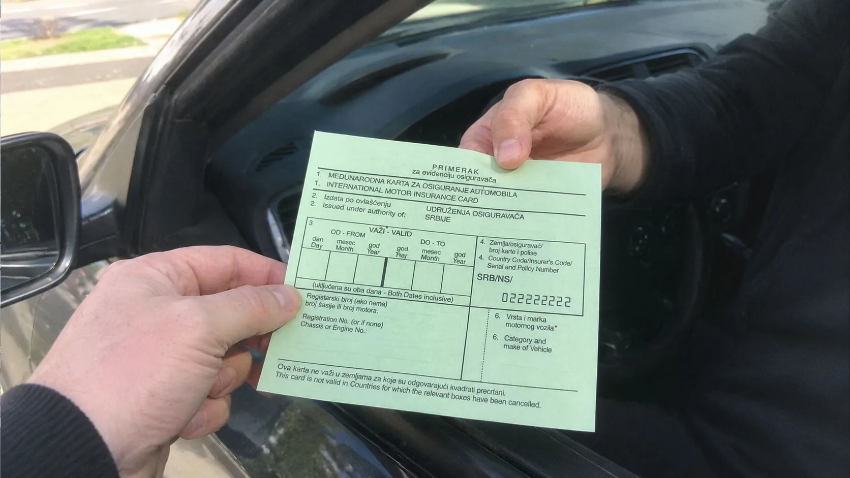 Zeleni karton, međunarodna karta osiguranja, u ruci pored prozora automobila