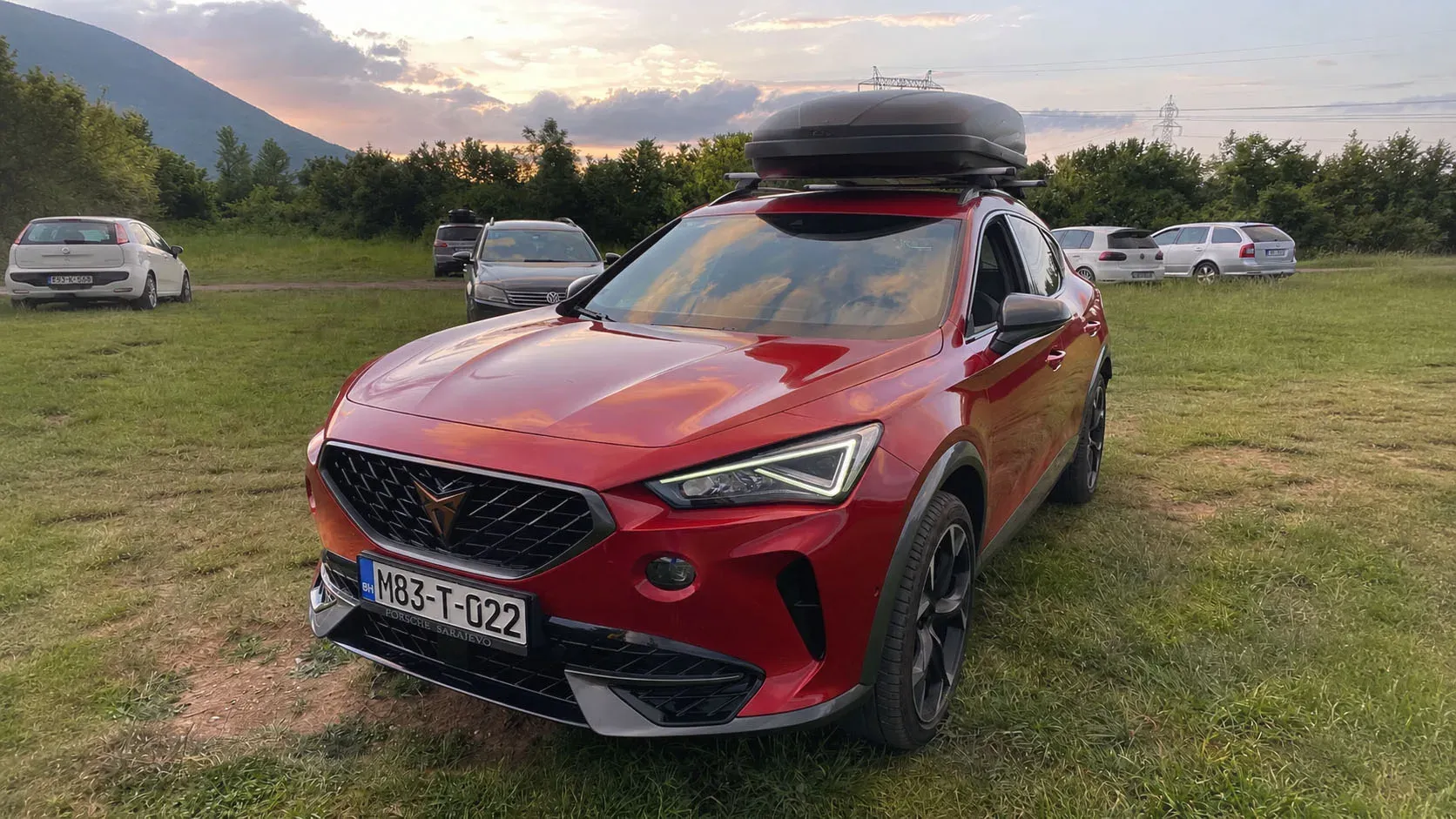SUV sa krovnim koferom parkiran na livadi u suton
