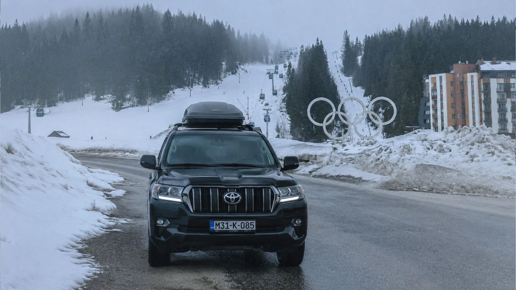 Iznajmljeni automobil kod olimpijskih krugova na Jahorini sa žičarom i skijalištem u pozadini